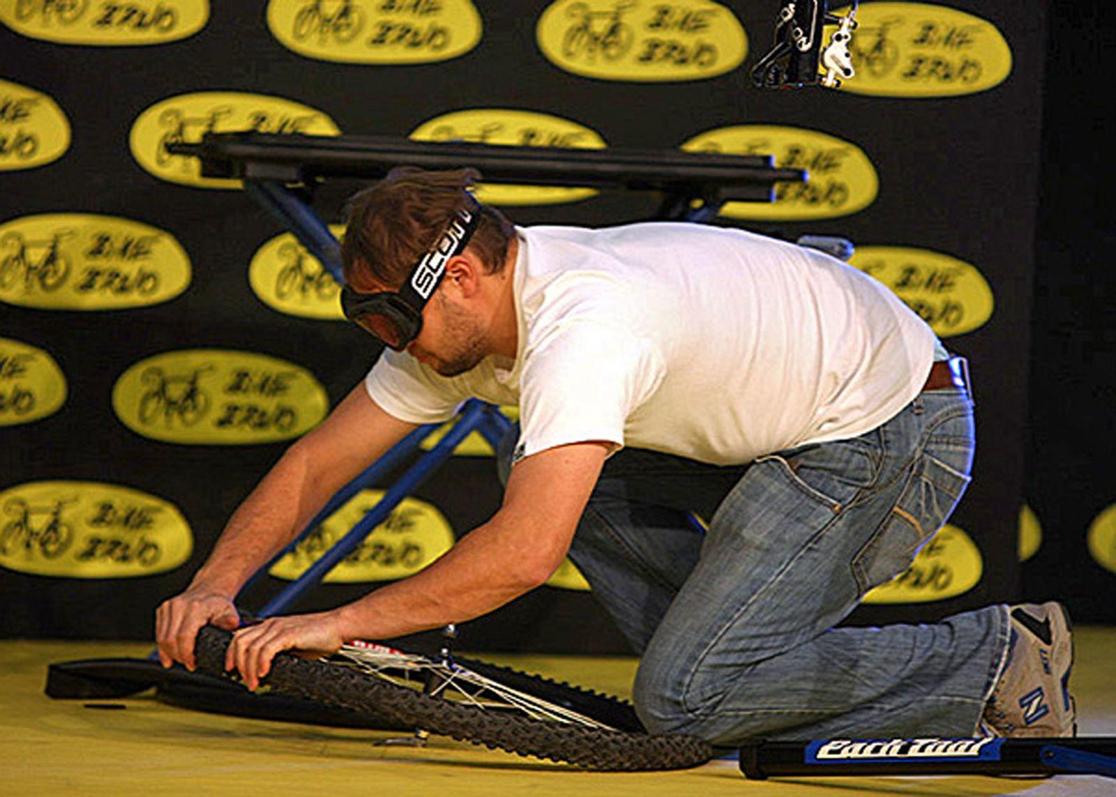 Man in white shirt and blackened ski goggled fixing a bicycle on the ground