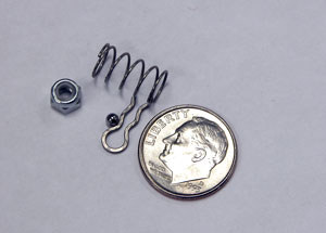 A 3/32-inch ball, small coil spring, a nut for a 3mm thread, a Shimano disc pad clip next to nickel