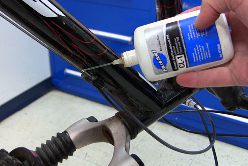 Tilted bike in repair stand as lubricant is dripped down the cables