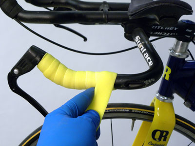 Gloved hand adding bright yellow handle bar tape to bike