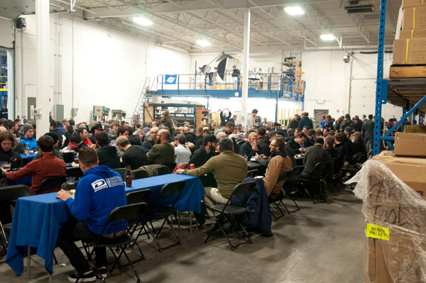 Large group sitting at tables in a large warehouse