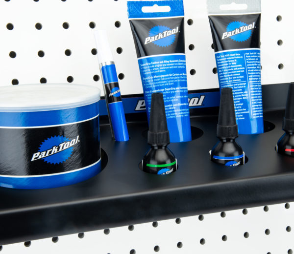 The Park Tool JH-2 Wall-Mounted Lubricant & Compound Organizer mounted to white pegboard holding lubricants, click to enlarge
