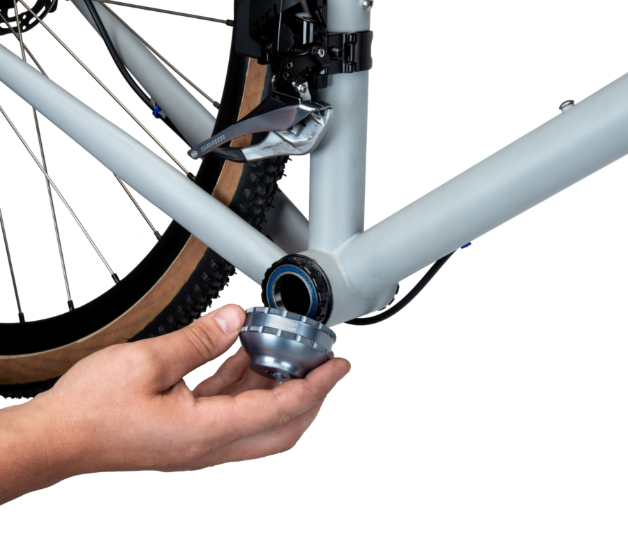 A hand fitting the BBT-27.3 Bottom Bracket Tool onto a black external bottom bracket cup on a gray bicycle, enlarged