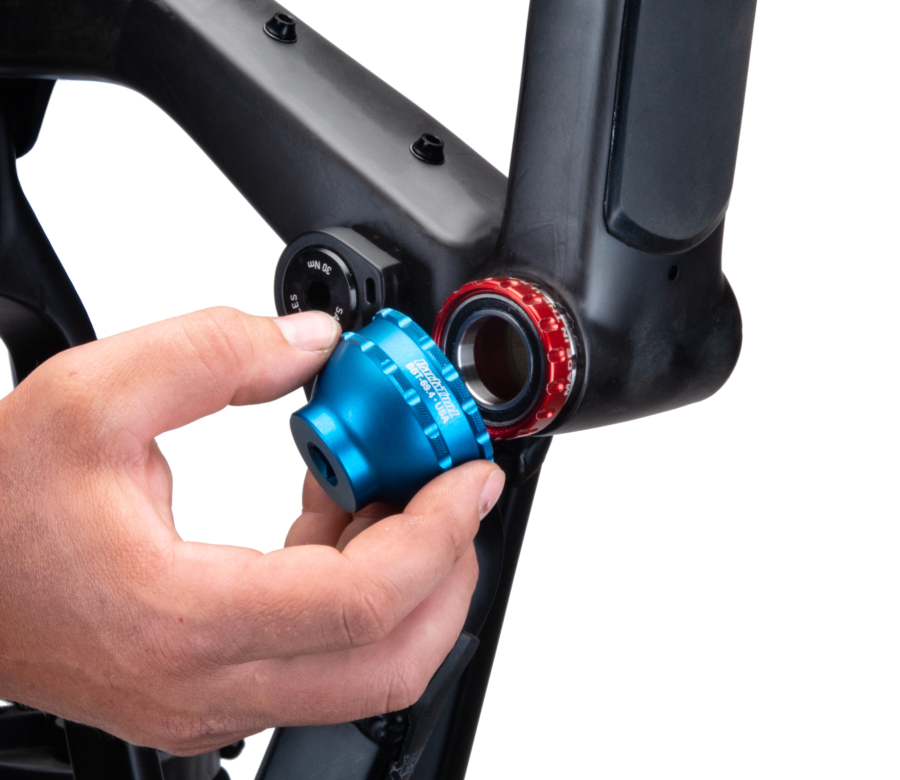 A hand fitting the BBT-69.4 Bottom Bracket Tool onto a red external bottom bracket cup on a black MTB frame, enlarged