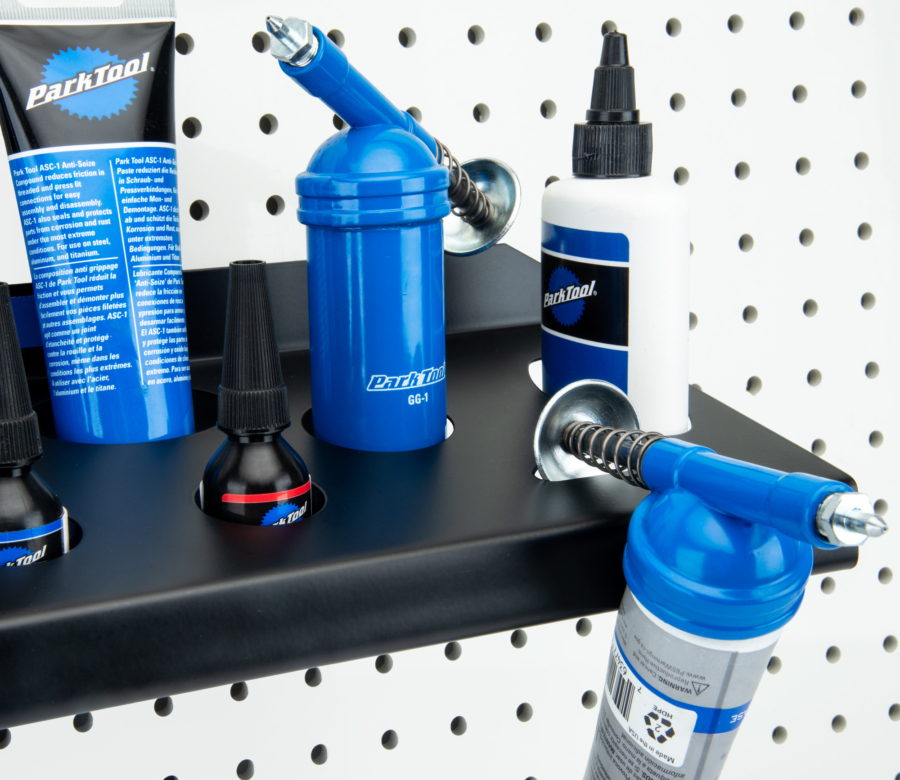 The Park Tool JH-2 Wall-Mounted Lubricant & Compound Organizer mounted to white pegboard holding lubricants, enlarged