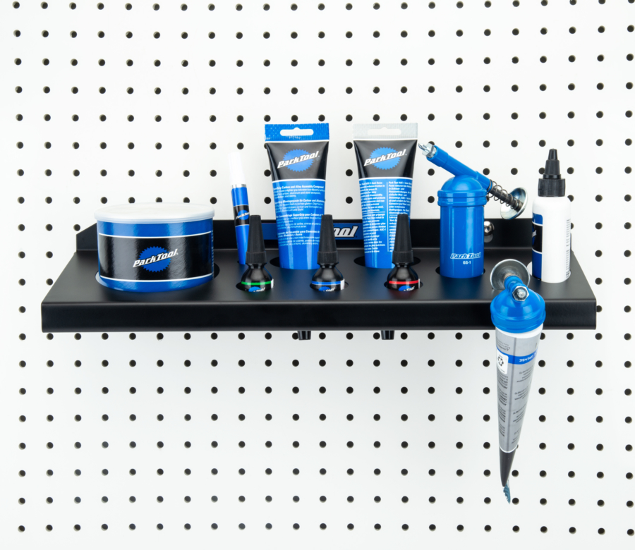 The Park Tool JH-2 Wall-Mounted Lubricant & Compound Organizer mounted to white pegboard holding lubricants, enlarged