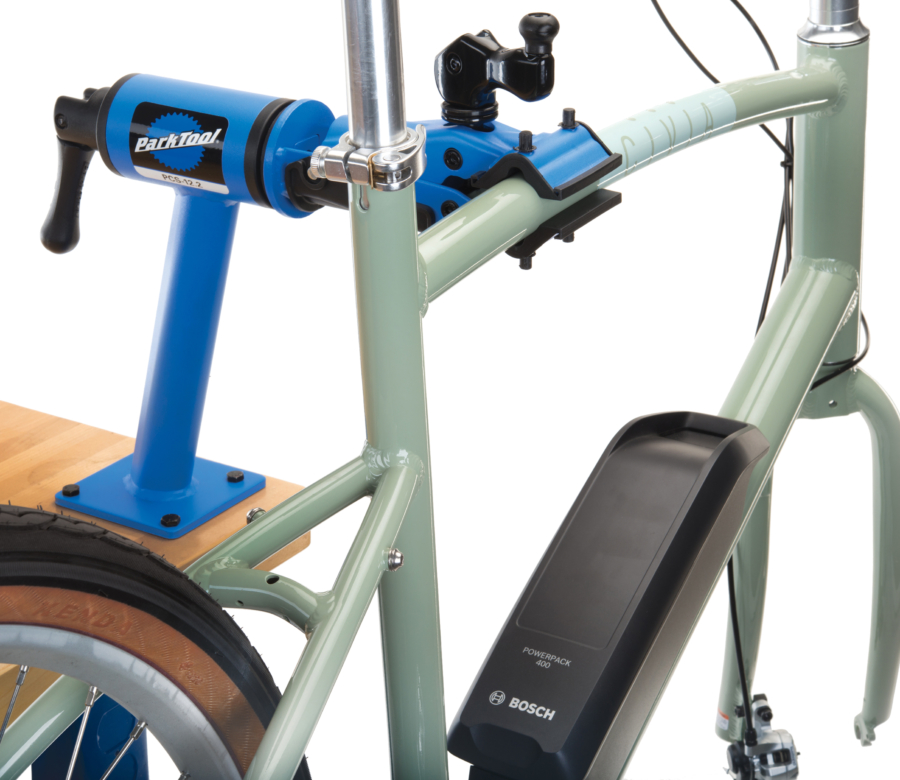 Park Tool PCS-12.2 Home Mechanic Bench Mount Repair Stand mounted to a maple workbench holding a green e-bike, enlarged