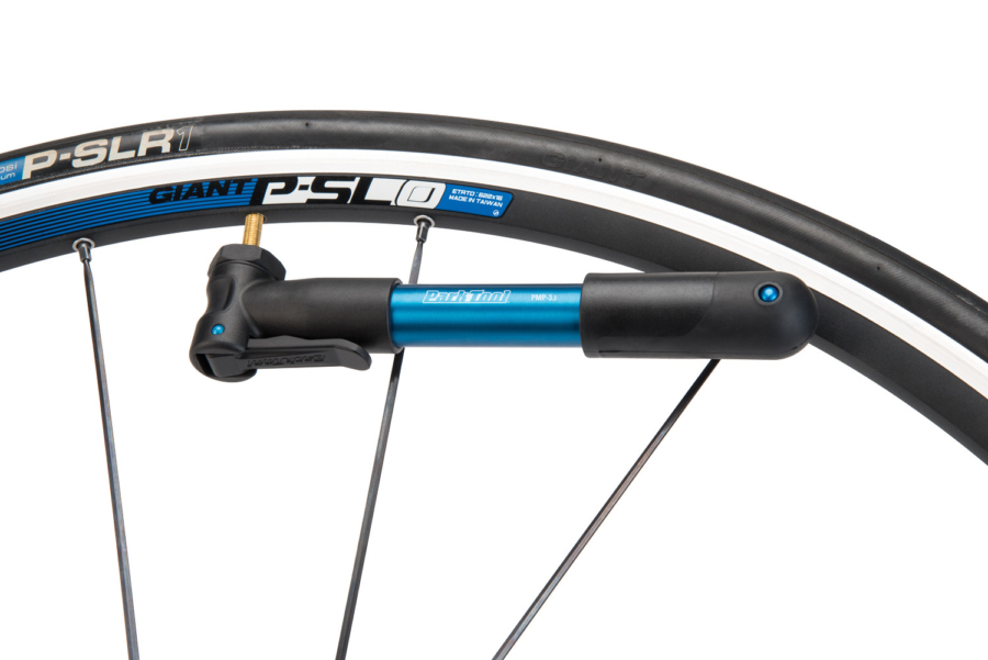 The Park Tool PMP-3.2 Micro Pump in blue placed onto Presta valve on road bike wheel, enlarged