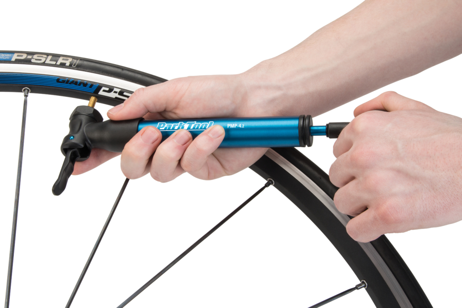 The Park Tool PMP-4.2 Mini Pump in blue being used on bike tire, enlarged