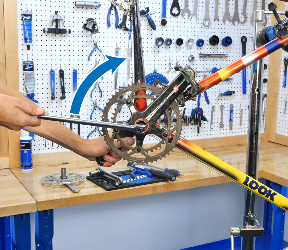Hex wrench turning crank bolt clockwise with hand holding non-drive side crank of bike in repair stand