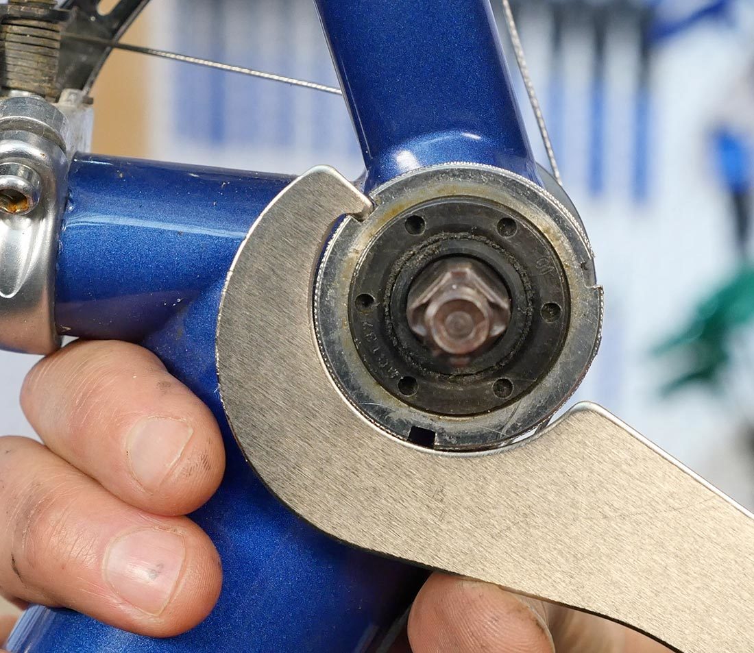 Bottom bracket lockring on a blue bicycle frame being loosened by an HCW-5