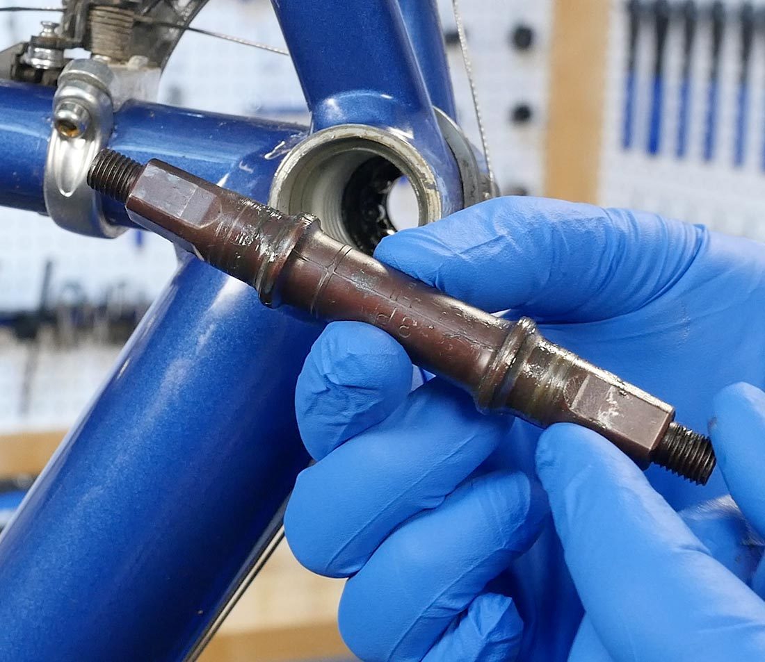 Spindle held in front of empty bottom bracket shell on a blue bicycle frame