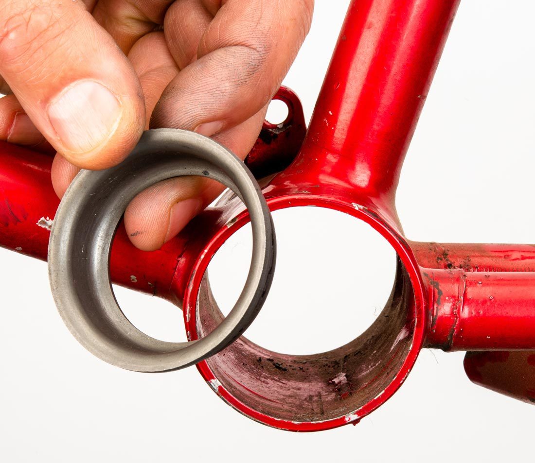 Ashtabula bearing cup held next to compatible bottom bracket shell on a red steel bike frame