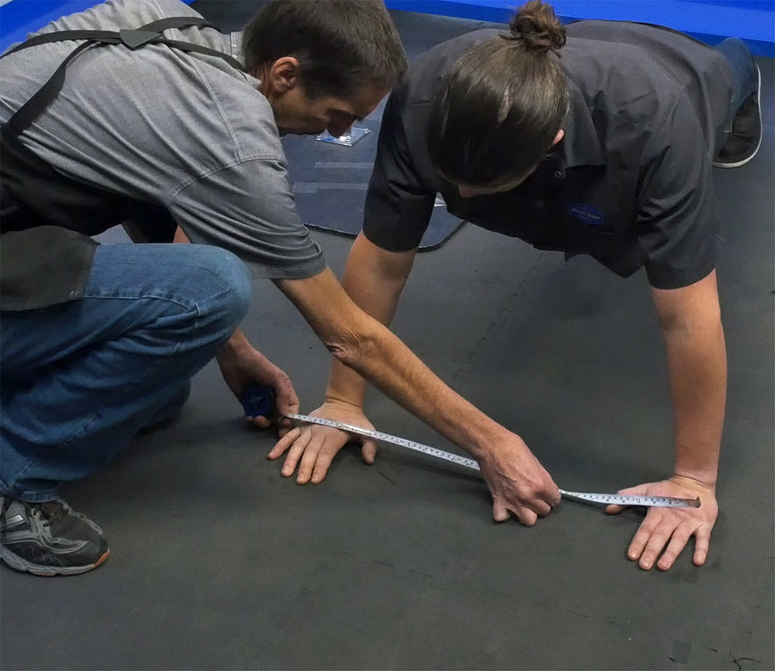 One person in a push-up position while another person measures the position of their hands