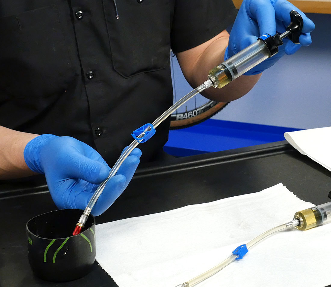 Bleed syringe being held with two hands with the hose end emptying used fluid into a waste container