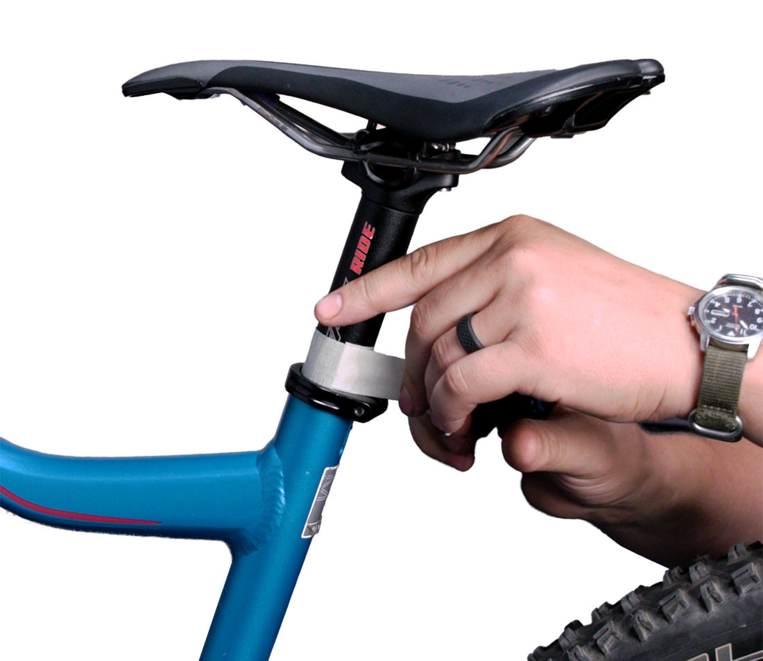 Hands applying masking tape to a bicycle seat post at the point where it meets the seat collar