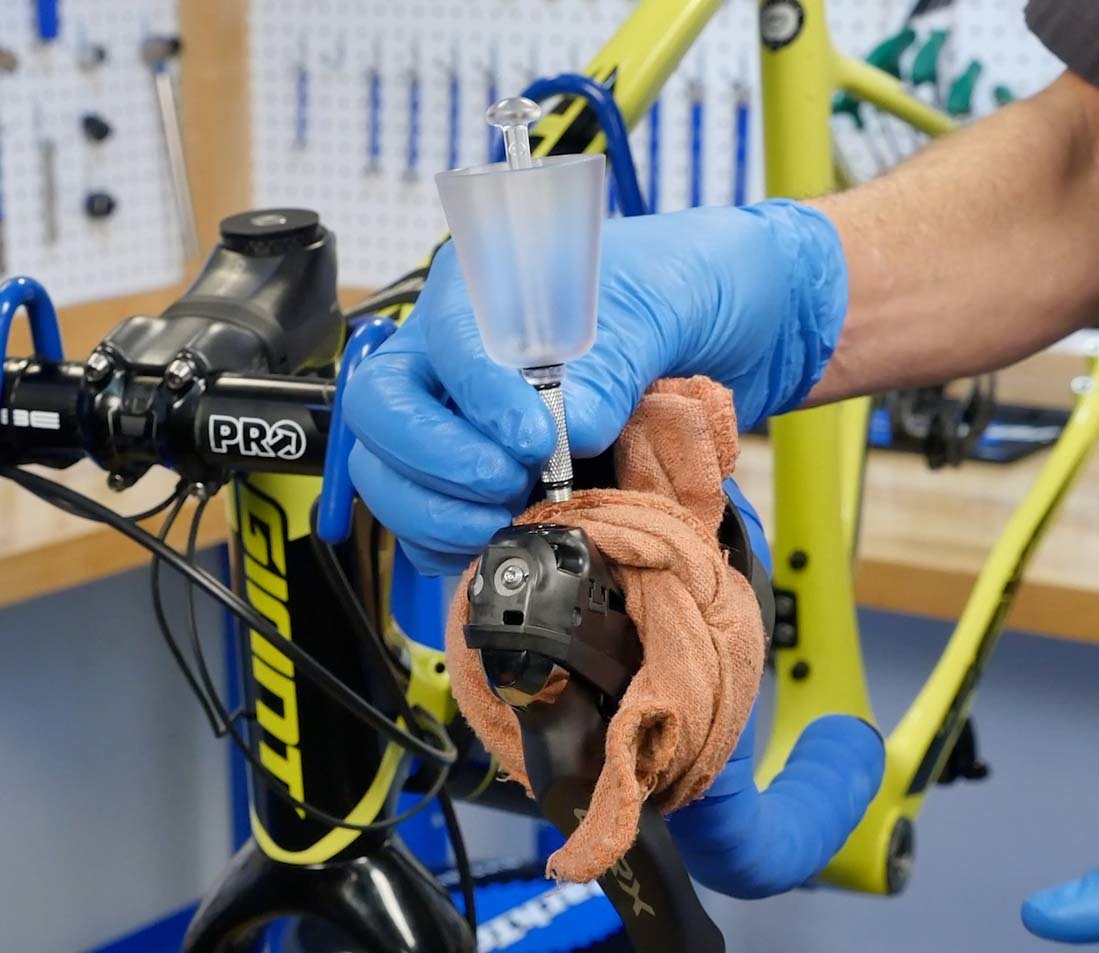 Hydraulic bleed funnel and extension being installed into brake levers on drop handlebars of a yellow bicycle
