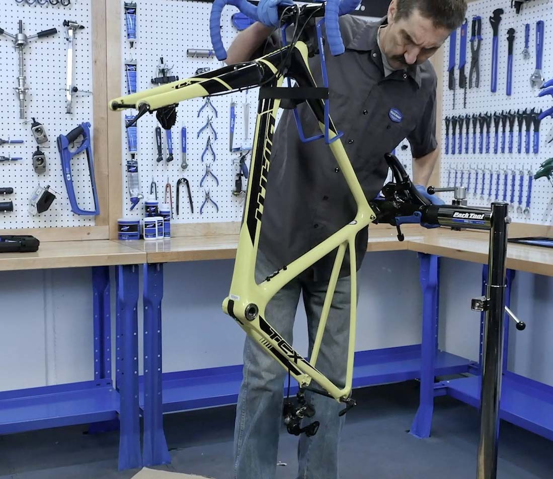 Yellow bicycle without wheels, held in shop repair stand clamp and tilted upward for bleeding