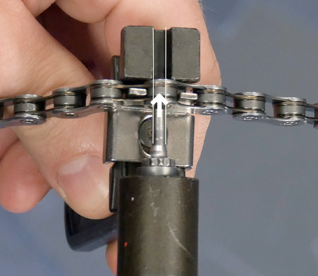 Closeup of chain tool with arrow demonstrating driving a chain rivet with the pin straight and centered